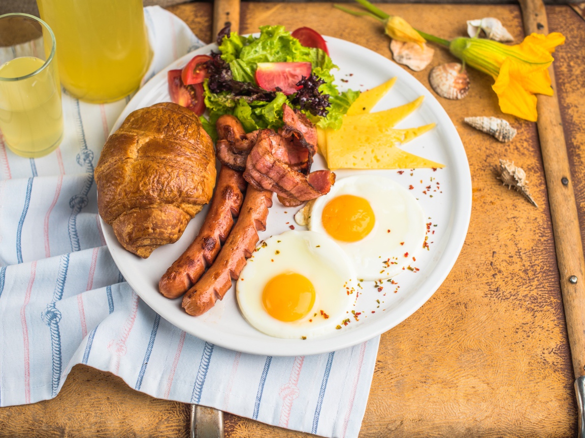 Яичница, салат, сосиски и круассан с соком на завтрак 