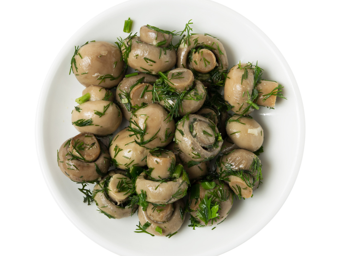 Маринованные шампиньоны с зеленью в белой тарелке на белом фоне 