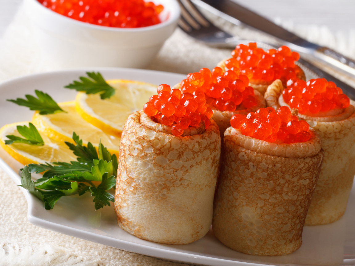 Блины с красной икрой на тарелке с лимонами и петрушкой