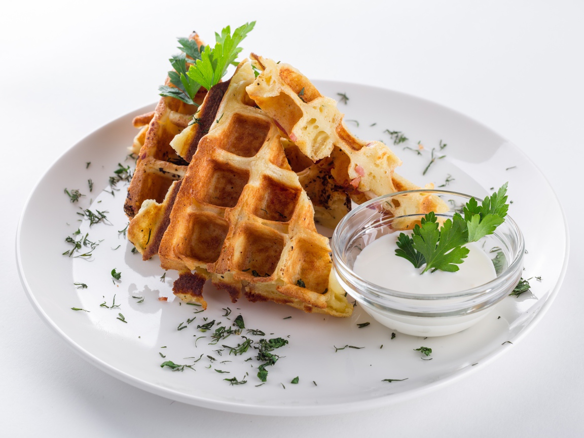 Несладкие вафли на белой тарелке с зеленью и соусом