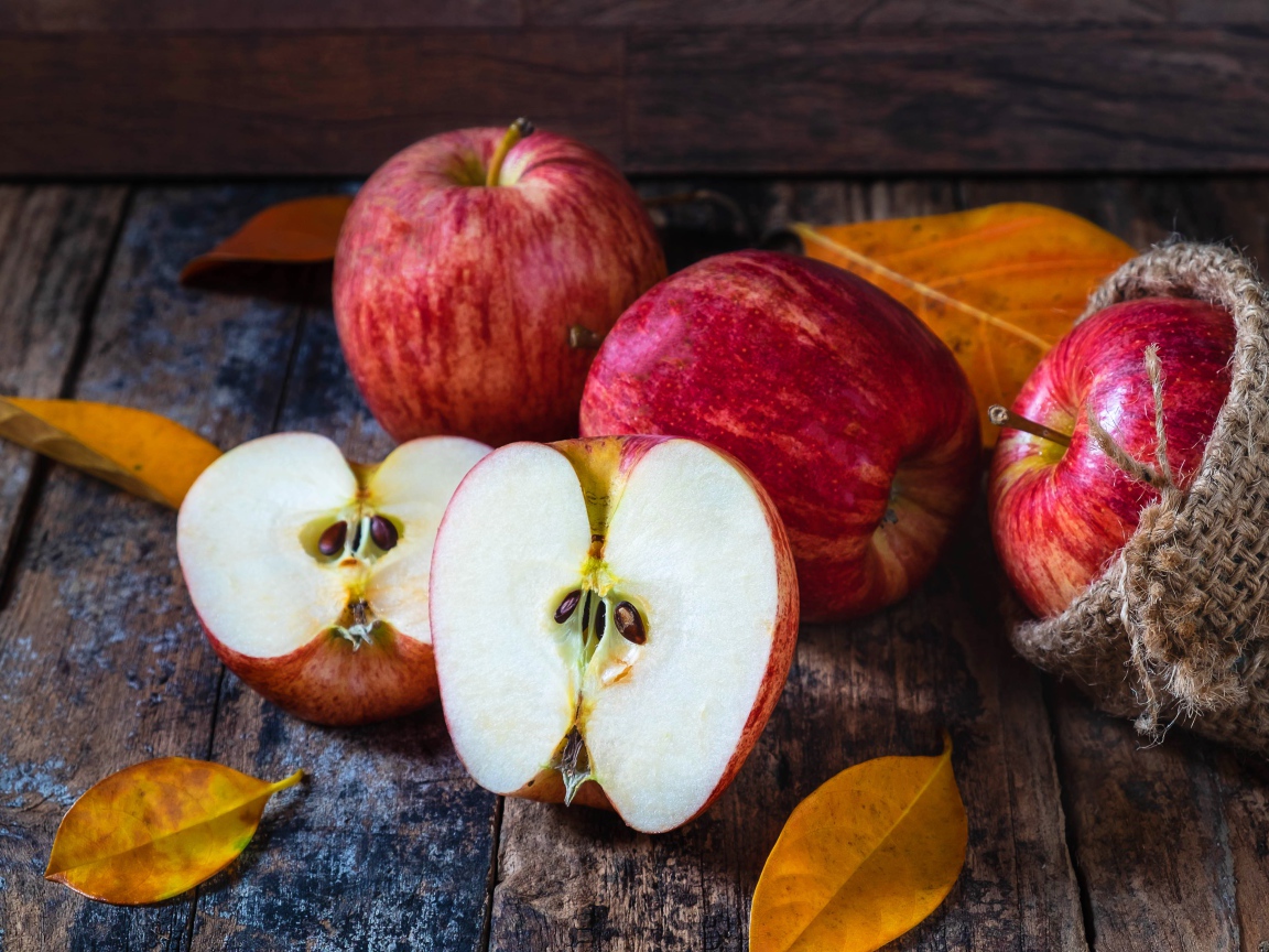 Красивые красные яблоки на столе с желтыми листьями