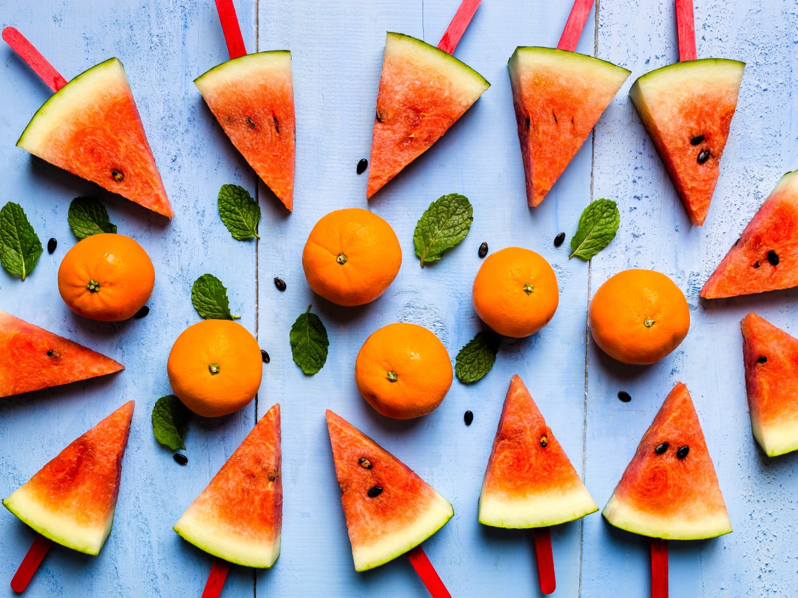 Кусочки арбуза на палочках на столе с мандаринами