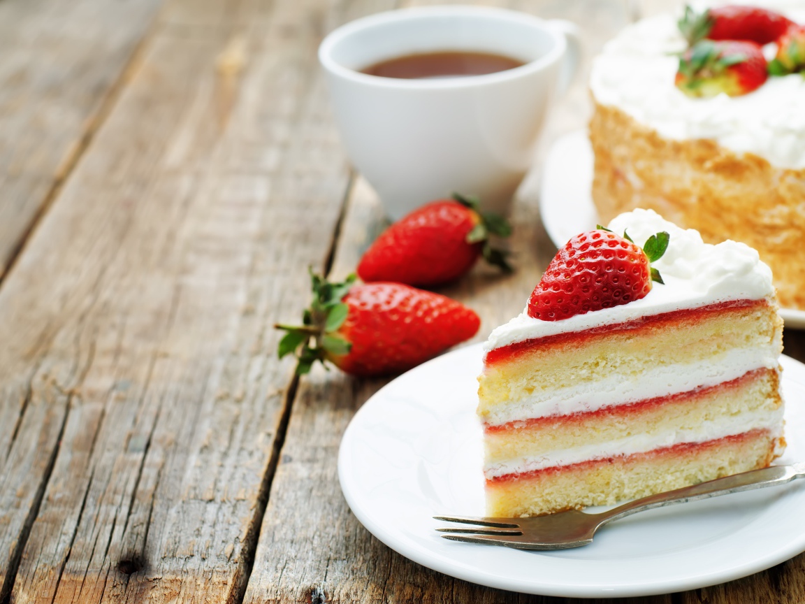 Кусок торта с клубникой на столе с чашкой чая 