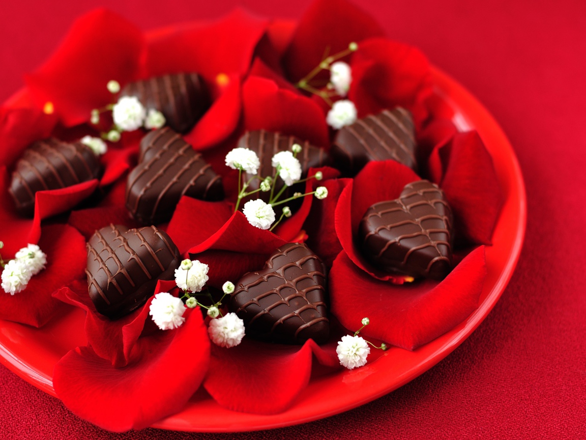 Шоколадные конфеты в форме сердца на тарелке с лепестками розы