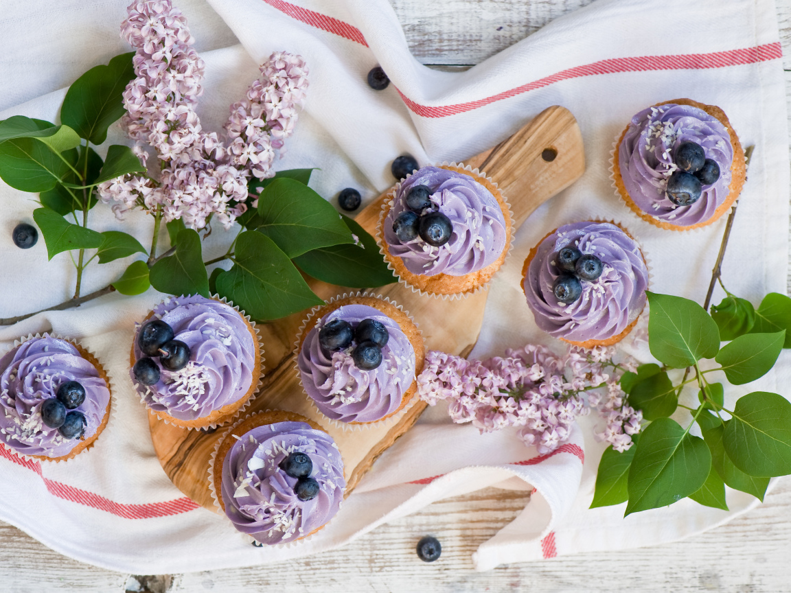 Кексы с кремом и ягодами черники на столе с ветками сирени 