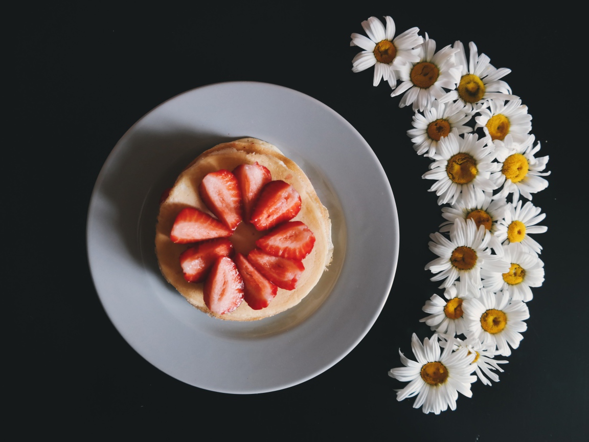 Оладьи с клубникой на тарелке на сером фоне с ромашками