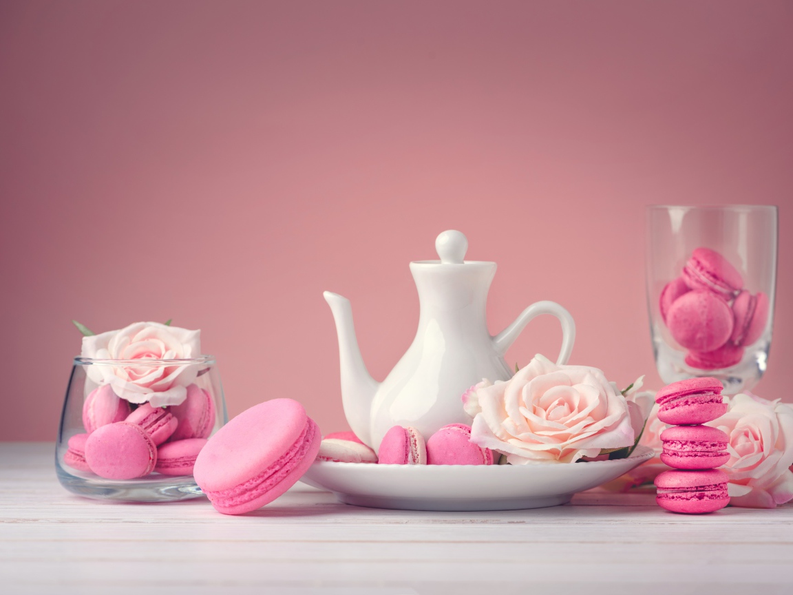 Розовый десерт макарун на столе с белый чайником и цветами розы