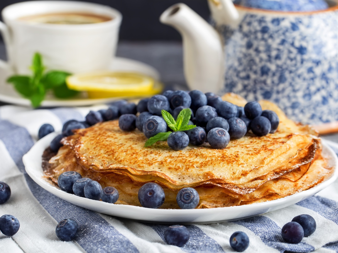 Тонкие блины с ягодами черники на столе с чаем