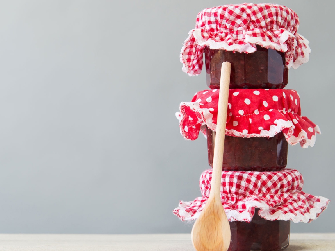 Три баночки варенья с деревянной ложкой на сером фоне