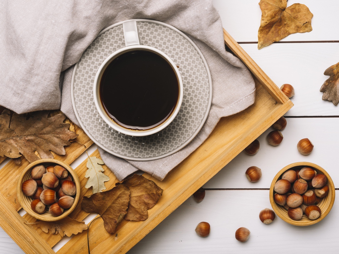 Чашка кофе на столе с лесными орехами и желтыми листьями
