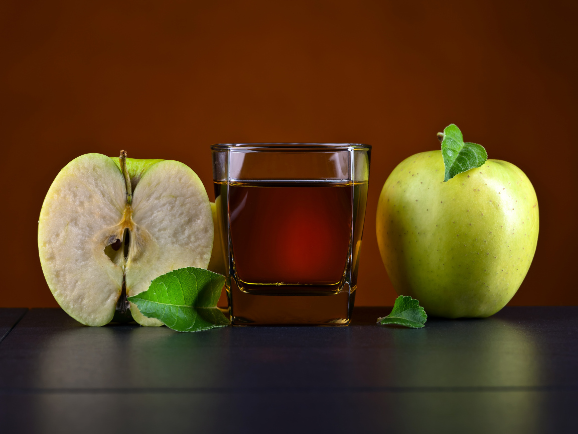Стакан яблочного сока на столе с зелеными яблоками