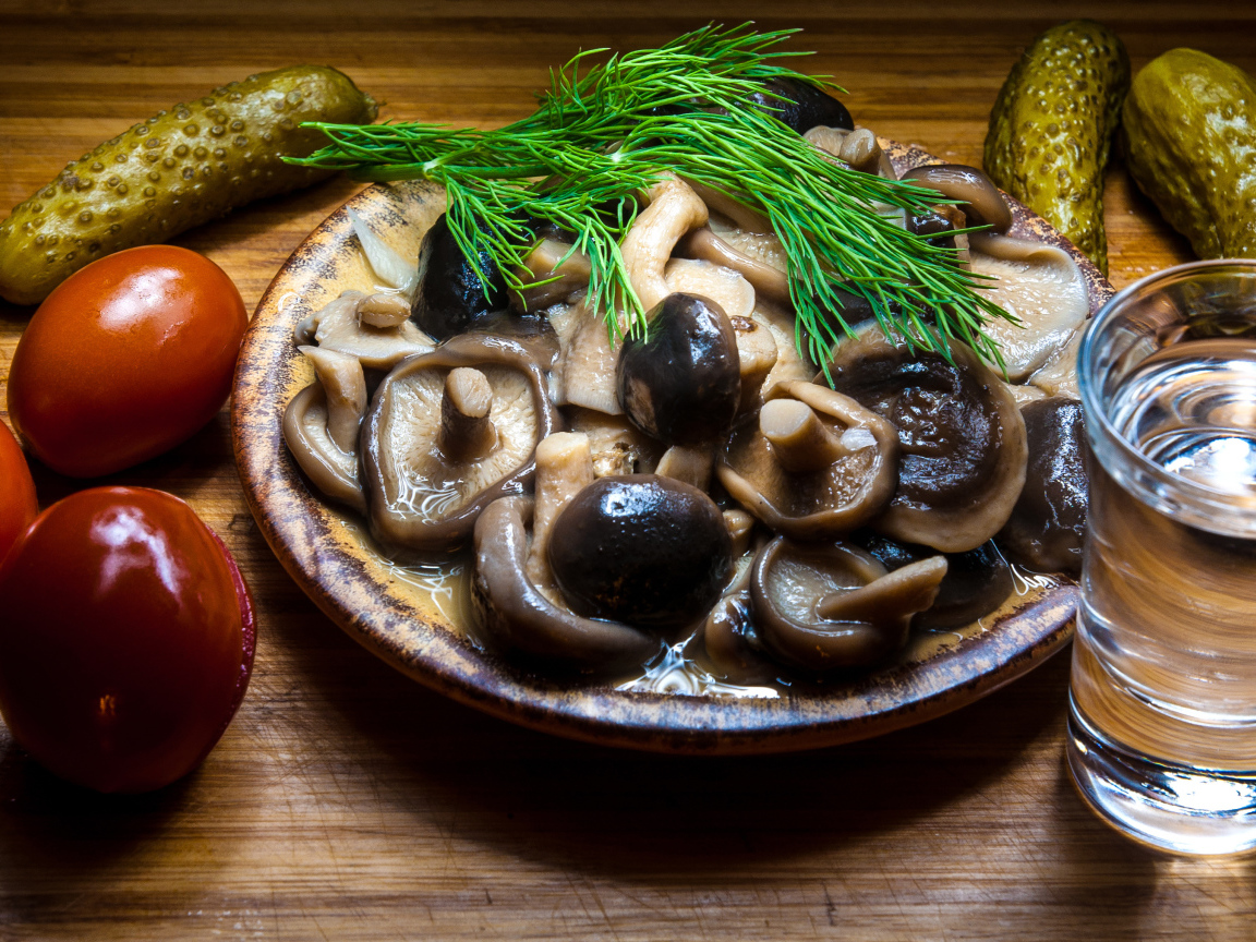 Рюмка водки на столе с солеными грибами, помидорами и огурцами