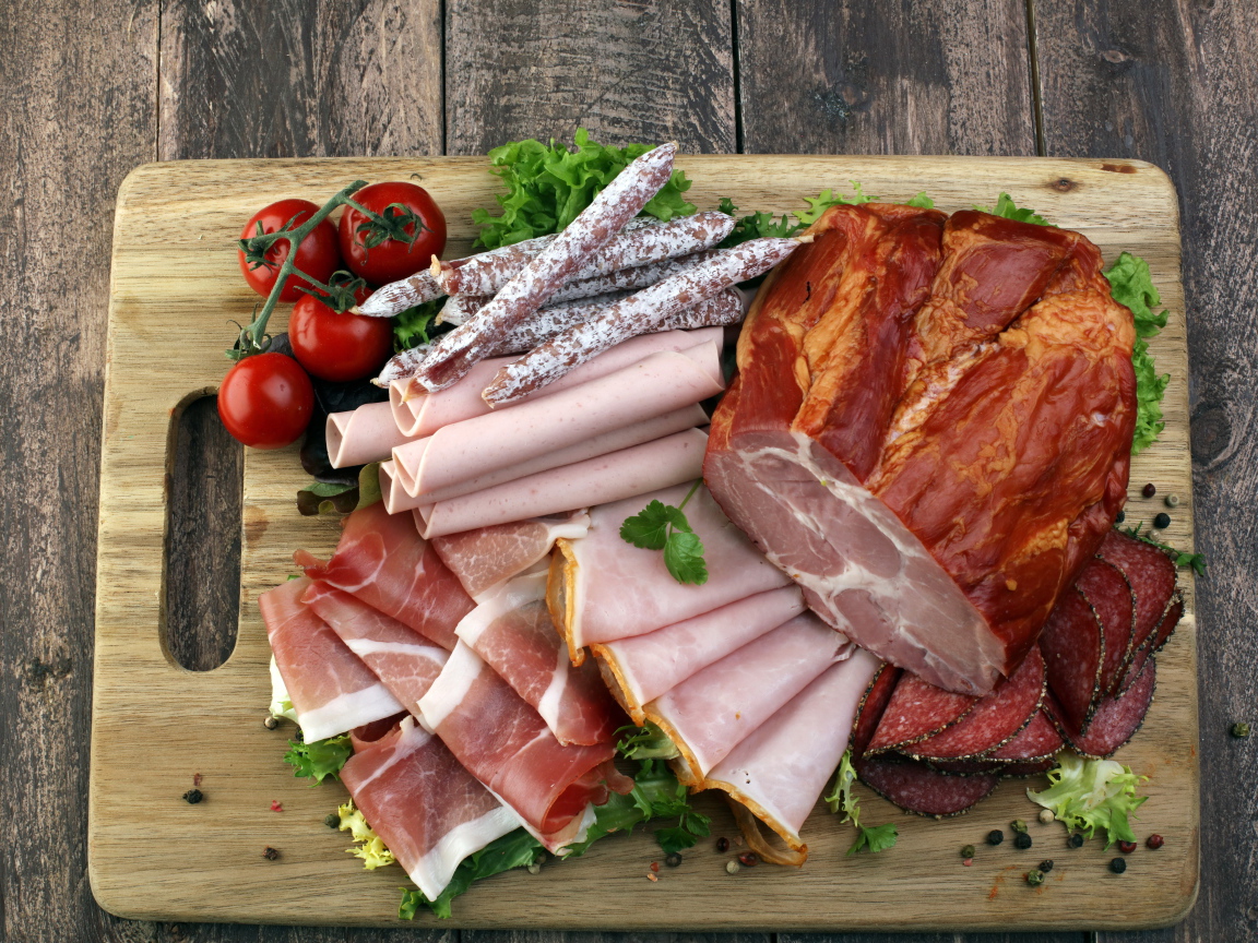 Мясная нарезка на разделочной доске с помидорами