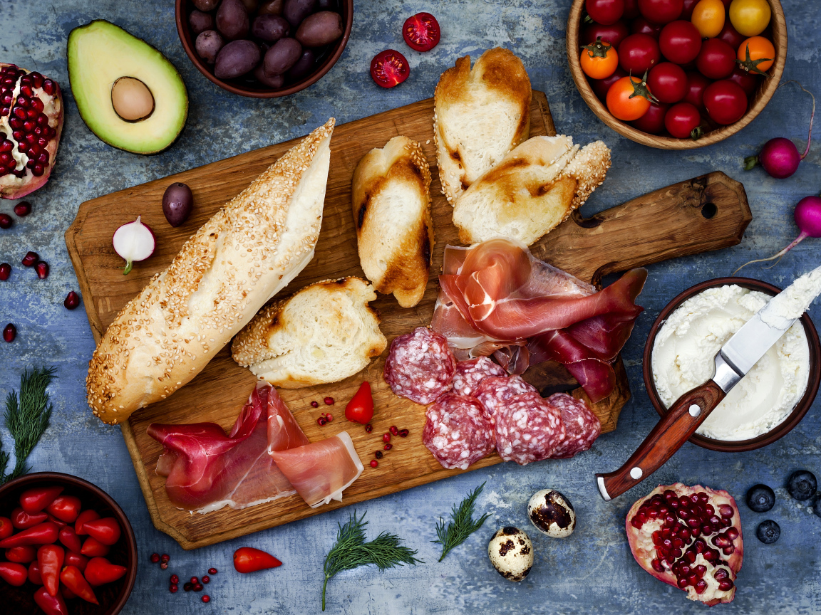 Мясные продукты с батоном и овощами на столе