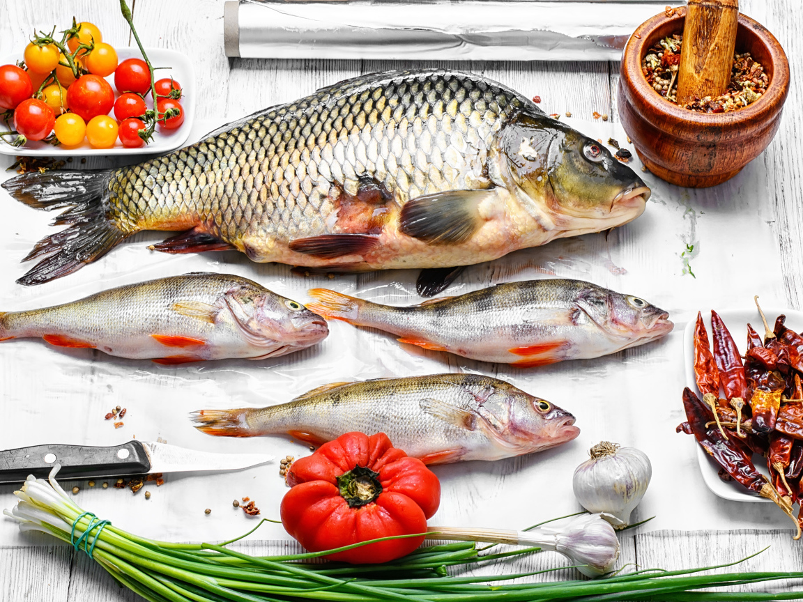 Свежая рыба на столе с помидорами, зеленым луком и  специями