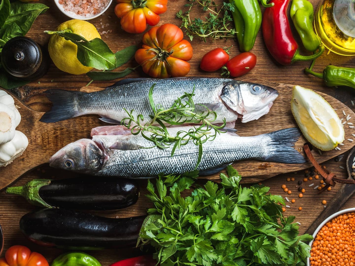 Свежая рыба на столе с овощами и зеленью 