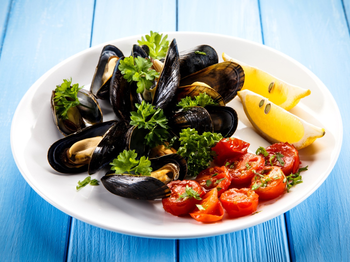 Мидии с томатами, кусочками лимона и зеленью петрушки на белой тарелке