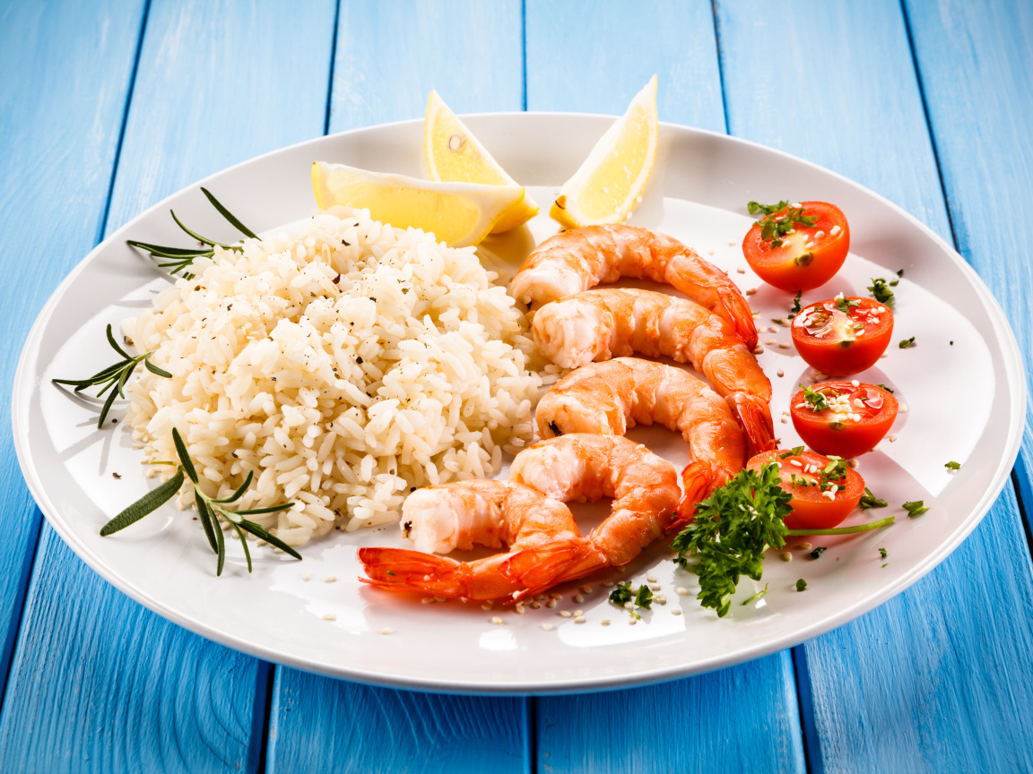 Креветки на тарелке с рисом, помидорами и лимоном