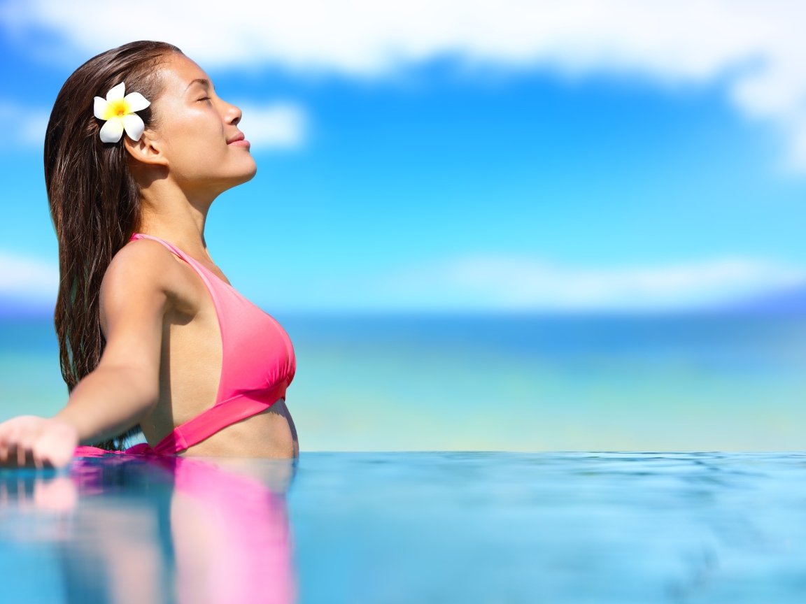 Девушка в розовом купальнике стоит в воде на солнце