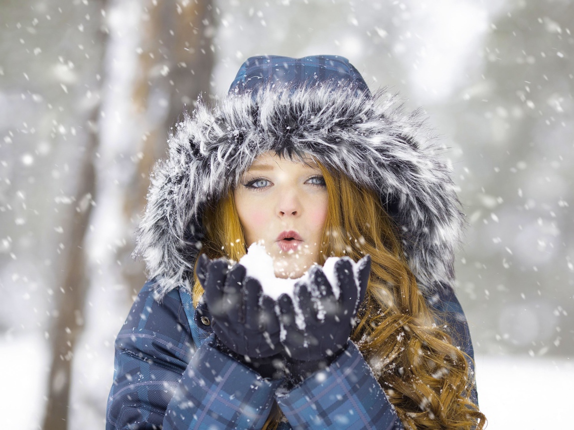 Красивая девушка в теплой куртке со снегом в руках