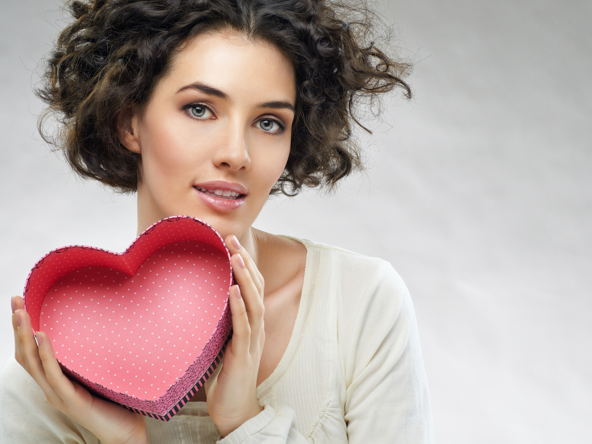 Красивая девушка с коробкой в форме сердца в руках на сером фоне