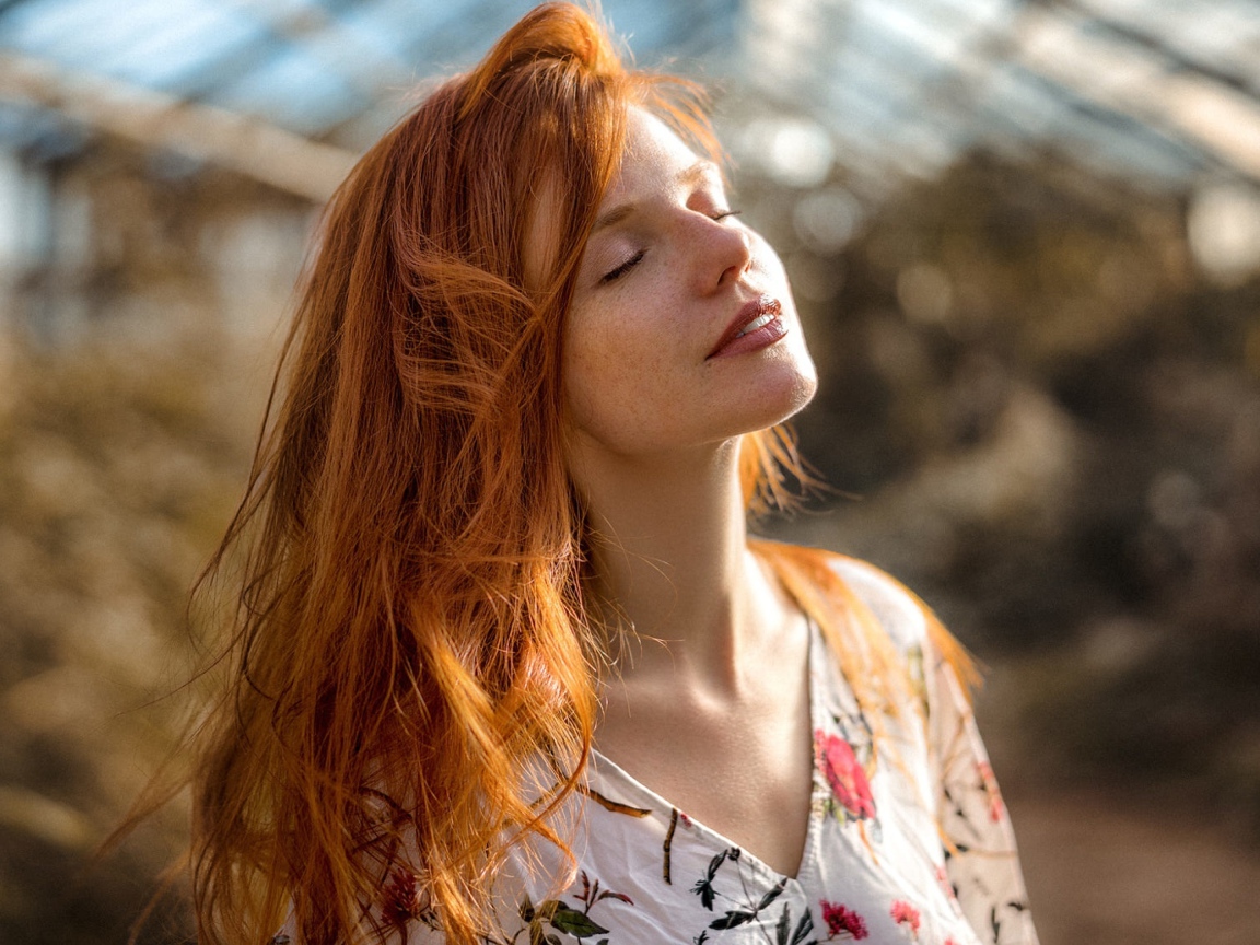 Красивая рыжеволосая девушка нежится в лучах солнца