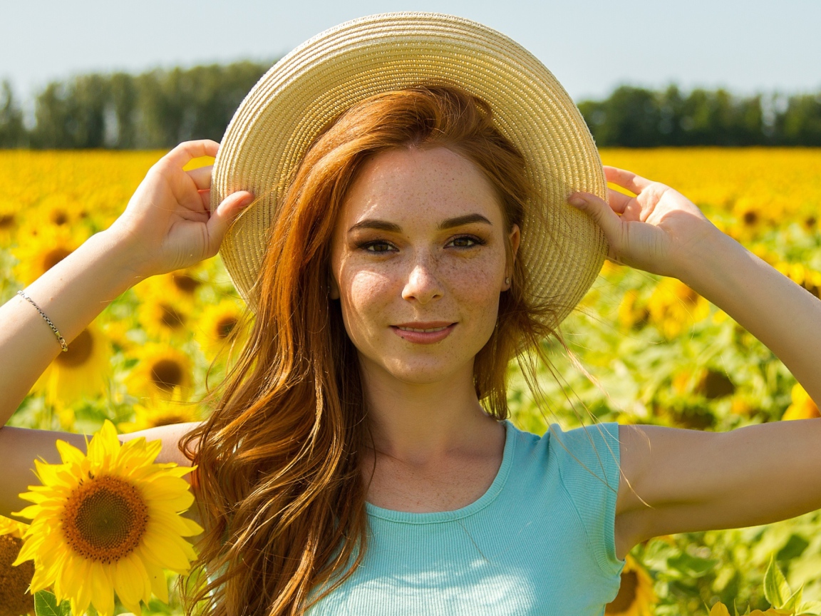 Красивая рыжеволосая девушка в шляпе на поле с подсолнухами 