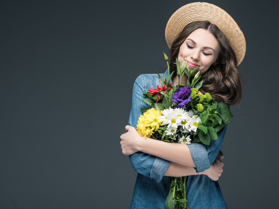 Красивая улыбающаяся девушка в шляпе с букетом цветов