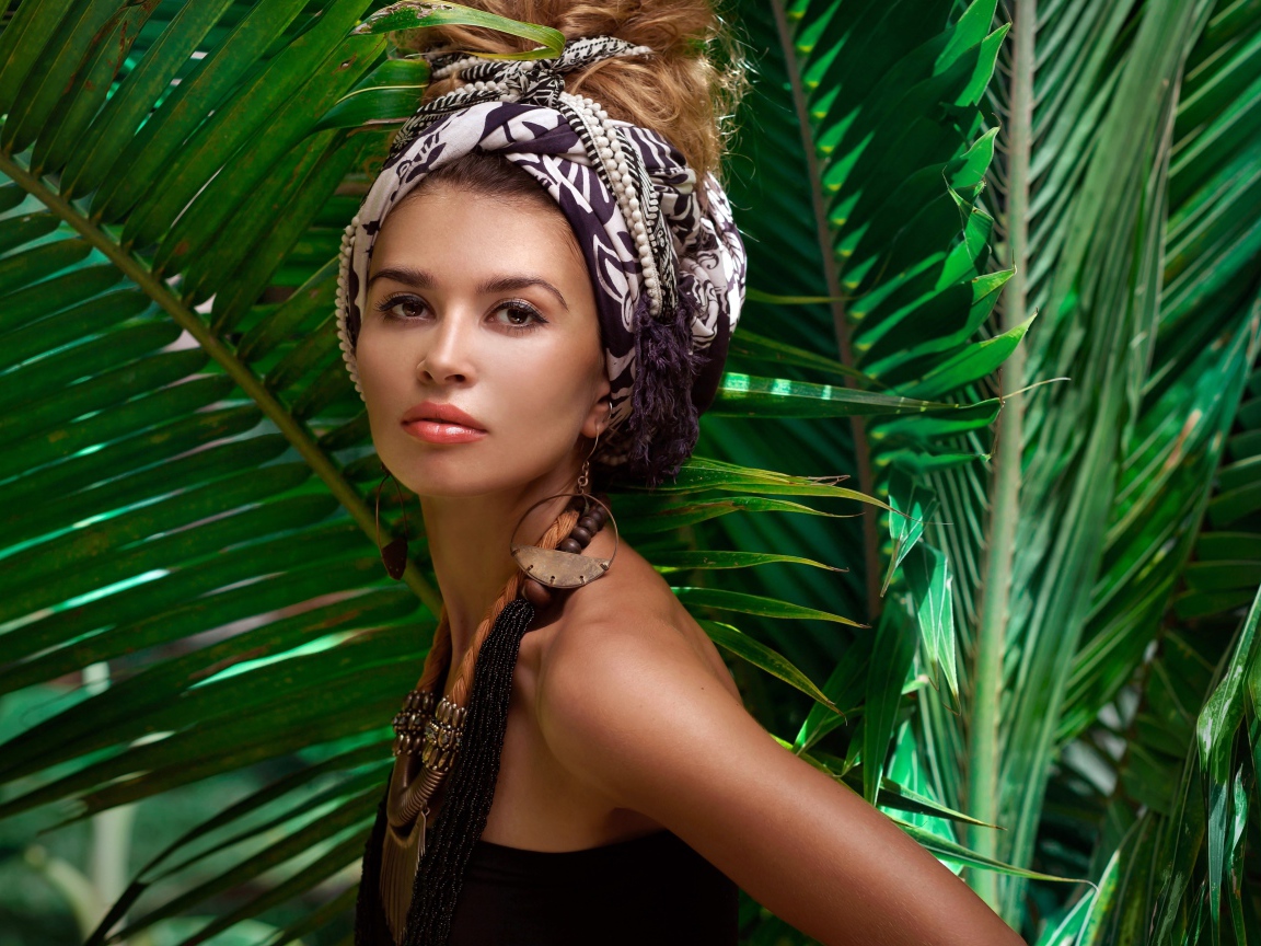 Красивая женщина в тюрбане с украшениями среди зеленых пальмовых листьев
