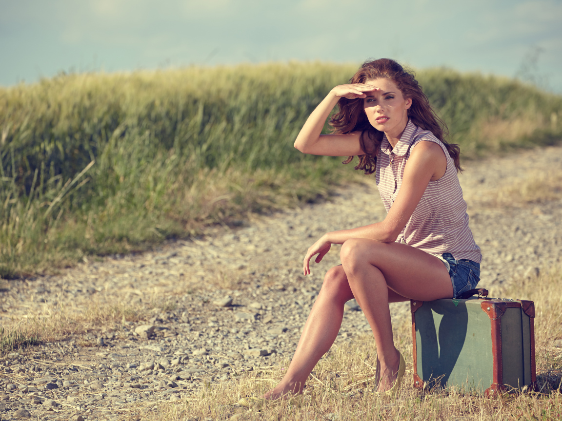 Красивая молодая девушка сидит на чемодане на дороге