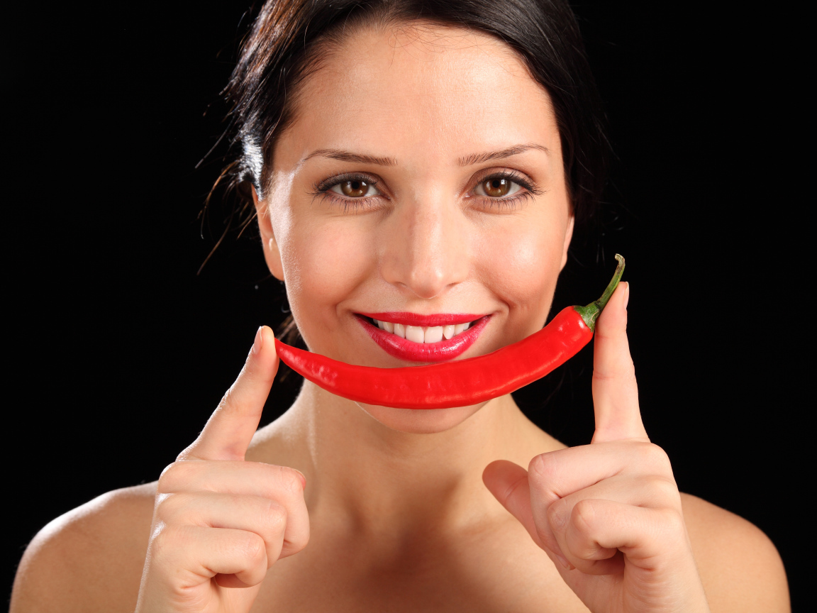 Улыбающаяся девушка с красным перцем на черном фоне