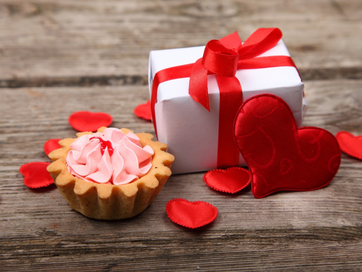 Пирожное, подарок и сердечки на деревянном фоне на День Святого Валентина