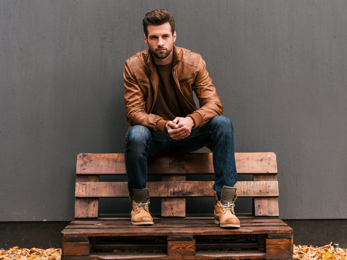 Молодой красивый мужчина сидит на деревянной лавке
