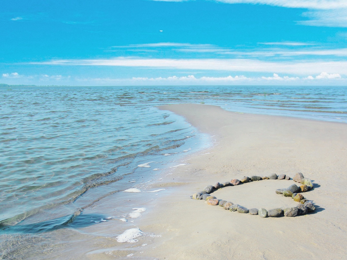 Сердце из камней на песке у спокойного моря под голубым небом