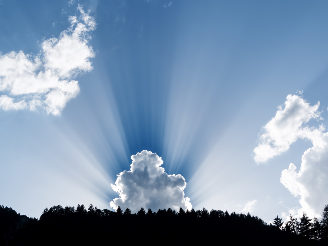 Лучи солнца пробиваются сквозь белые облака в голубом небе 