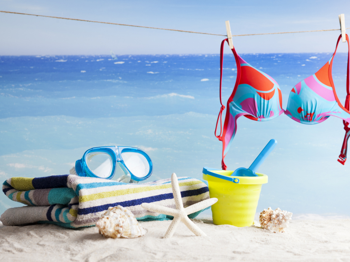 Очки, купальник, полотенце, ракушки и игрушки на песке на пляже летом