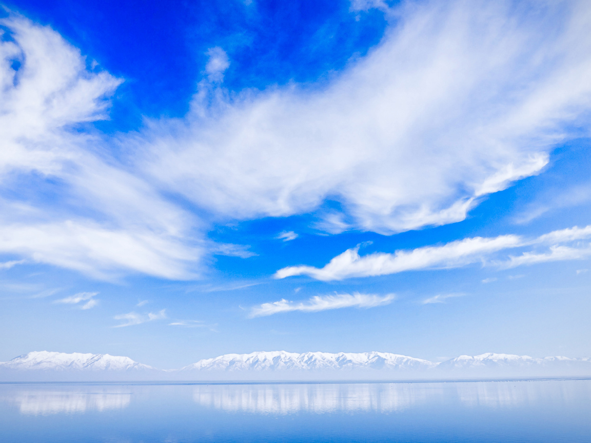 Красивые белые облака над водой около заснеженных гор