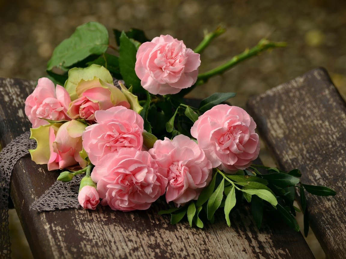 Букет красивых нежных розовых роз лежит на деревянной лавке