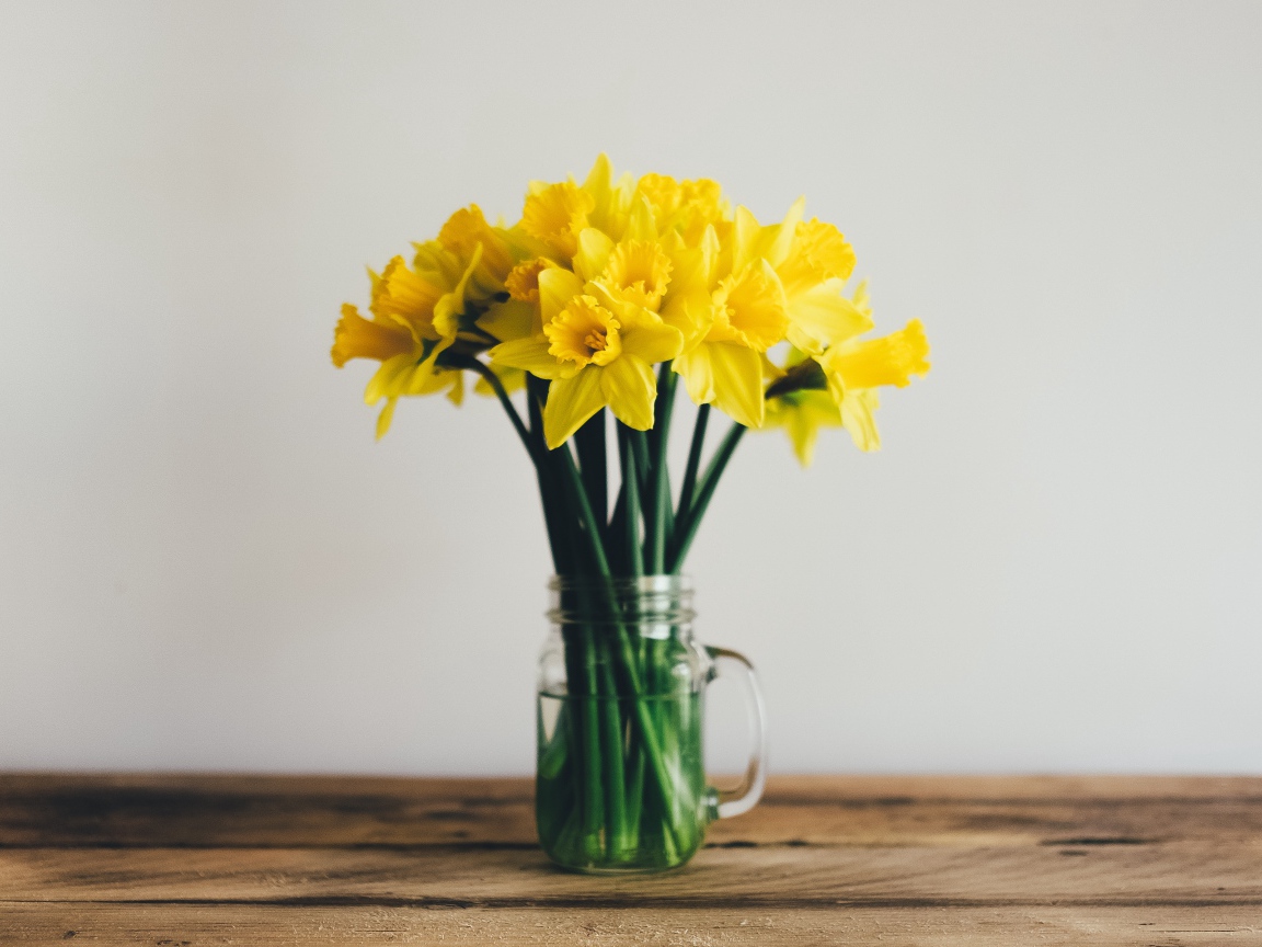 Букет желтых нарциссов в стеклянной вазе на столе 