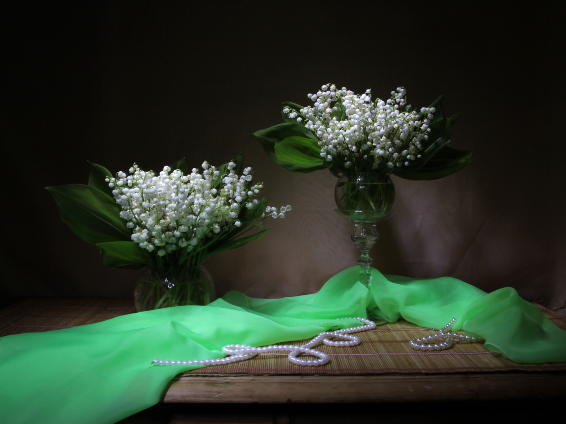 Два букета ландышей с бусами на столе 