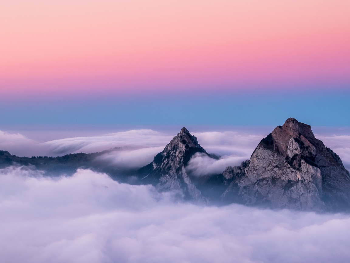 Верхушки гор в белых облаках под красивым розовым небом 