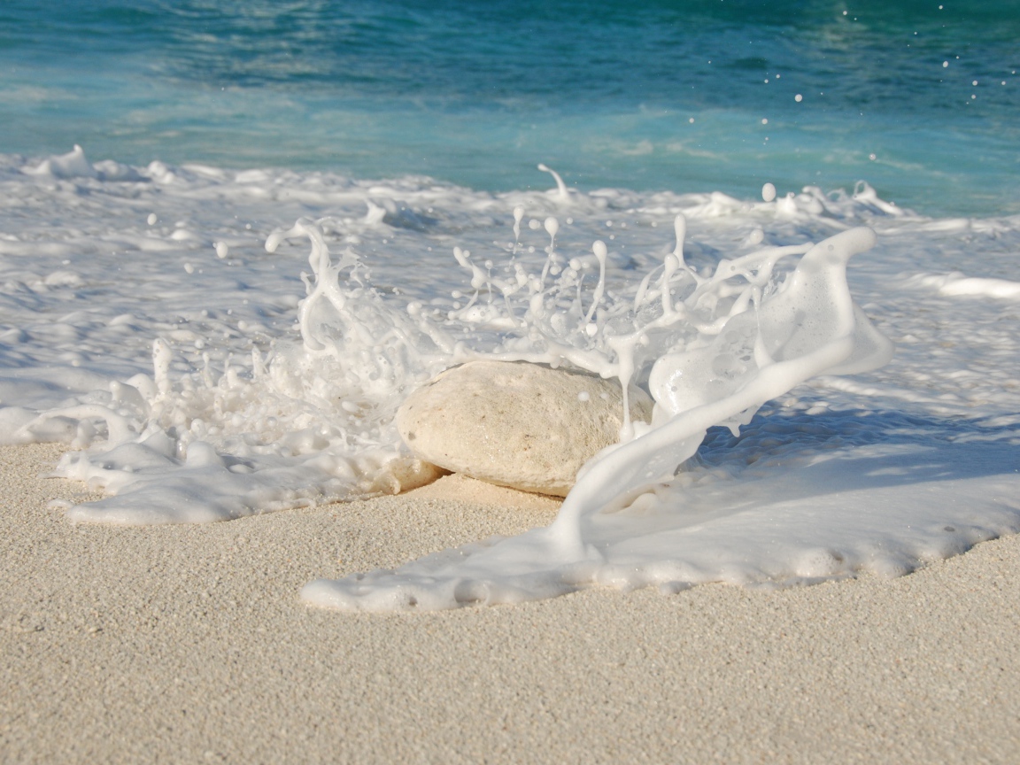 Белые морские волны бьются об камень на желтом песке