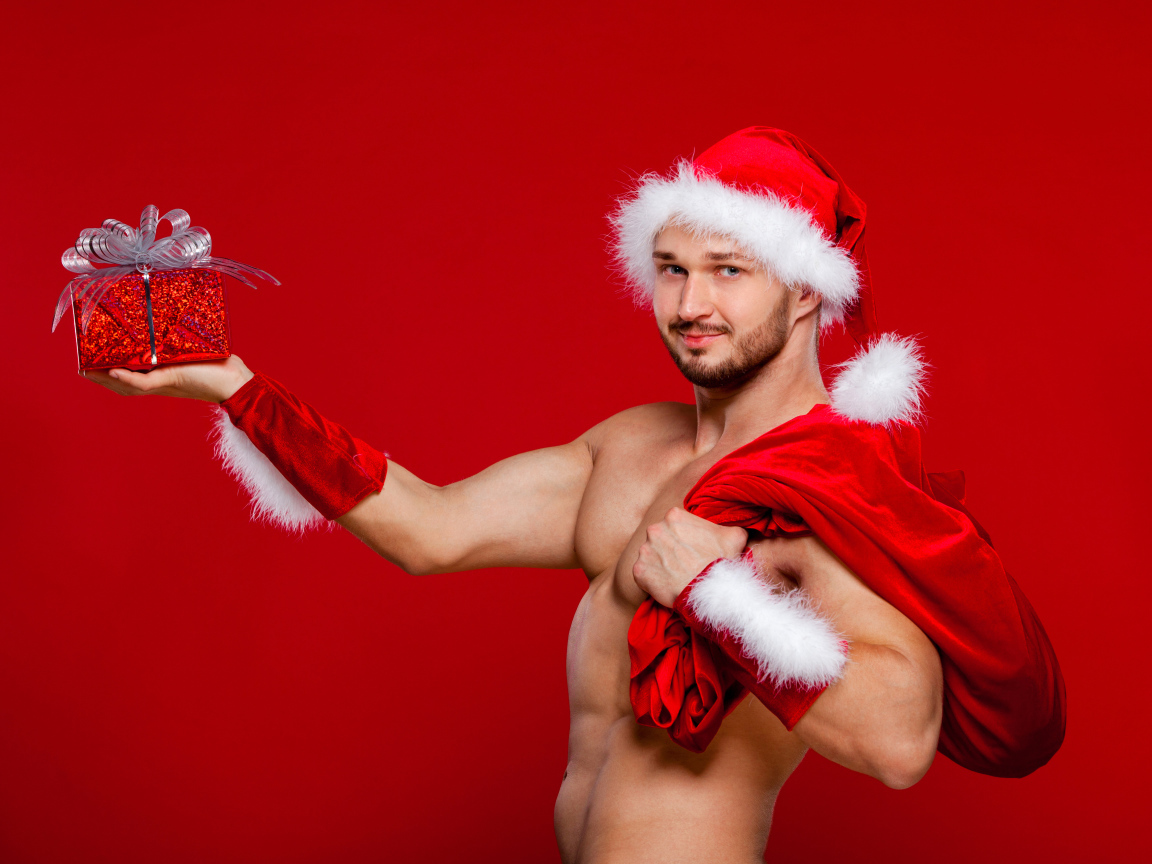 Мужчина в новогоднем костюме Санта Клауса с мешком и подарком в руке на красном фоне