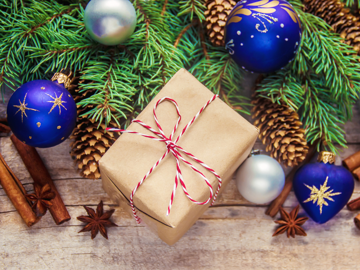 Еловая ветка с игрушками на столе с корицей и подарком на Новый год 