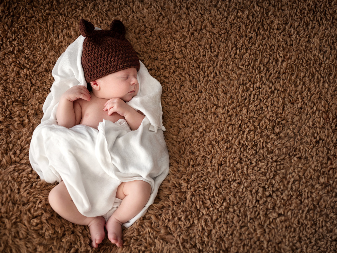 Грудной ребенок в вязаной шапке  спит в белом покрывале 