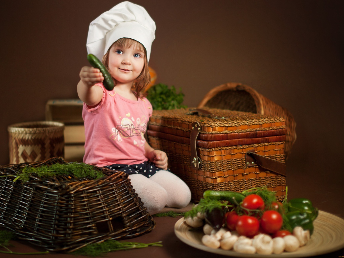 Маленькая девочка в шапке повара с огурцом в руках
