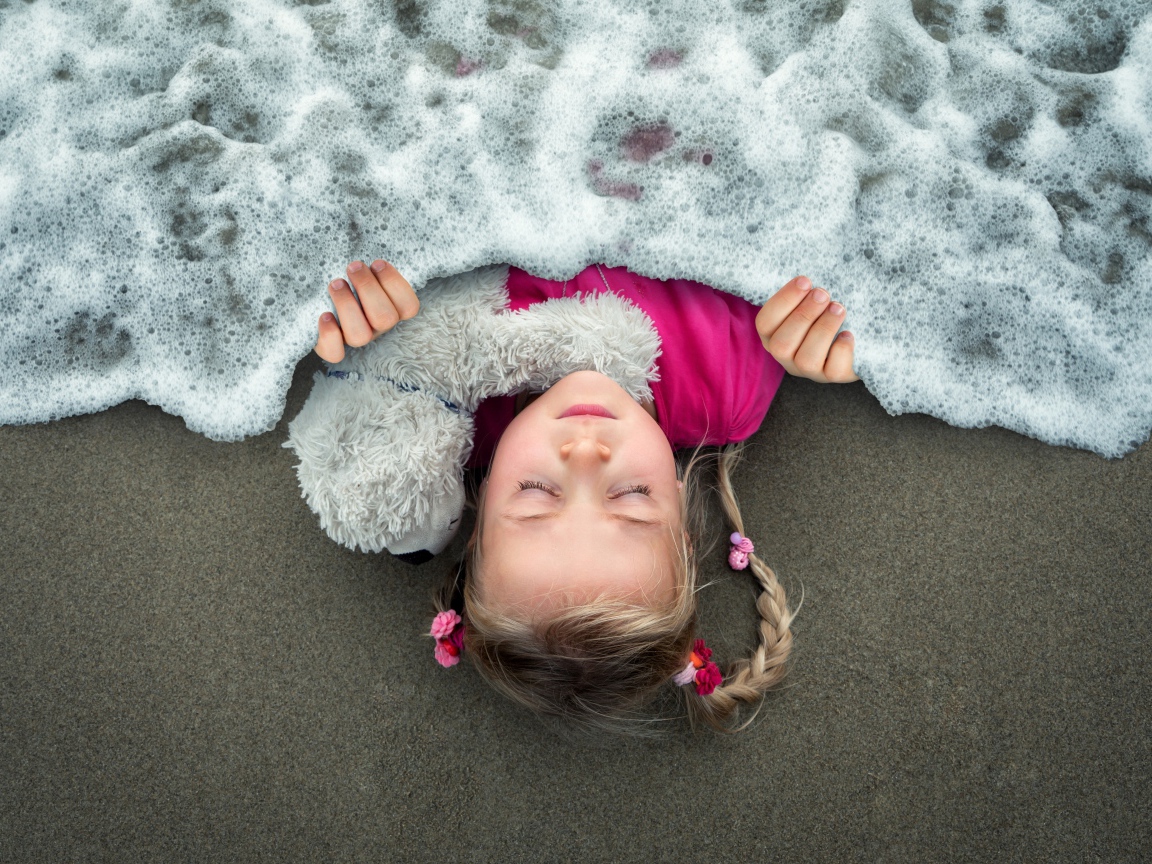 Маленькая девочка спит на песке под одеялом из морской пены