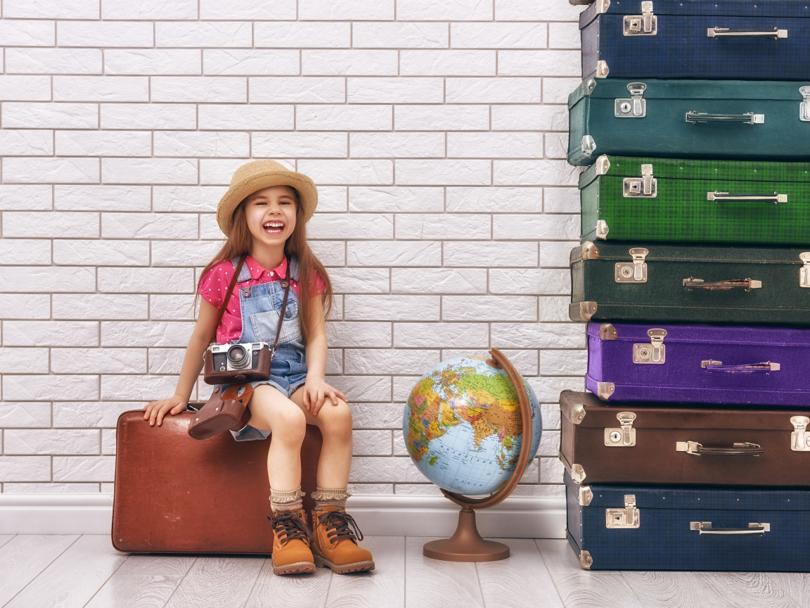 Маленькая девочка с фотоаппаратом сидит на чемодане
