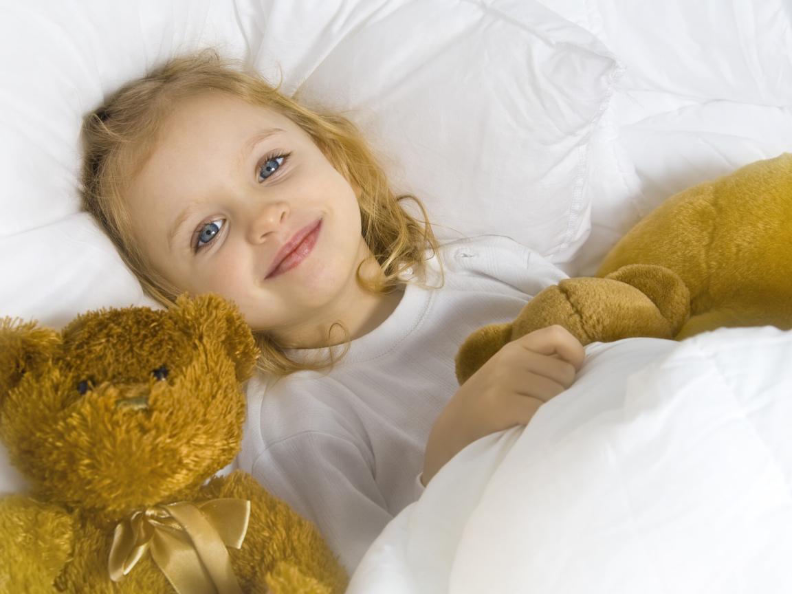 Милая голубоглазая девочка с мягкими игрушками лежит под одеялом