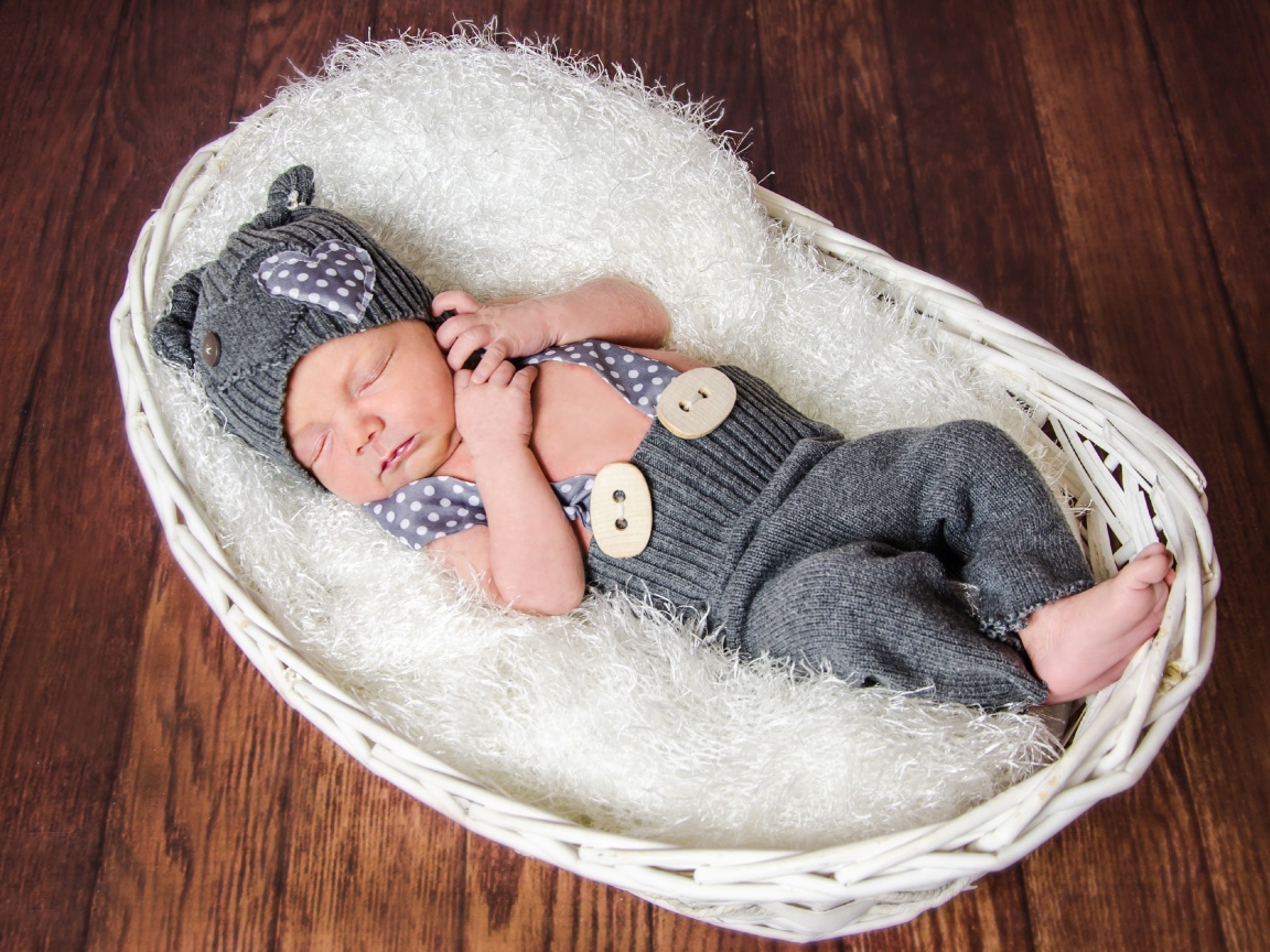 Спящий младенец в сером костюме в белой корзине